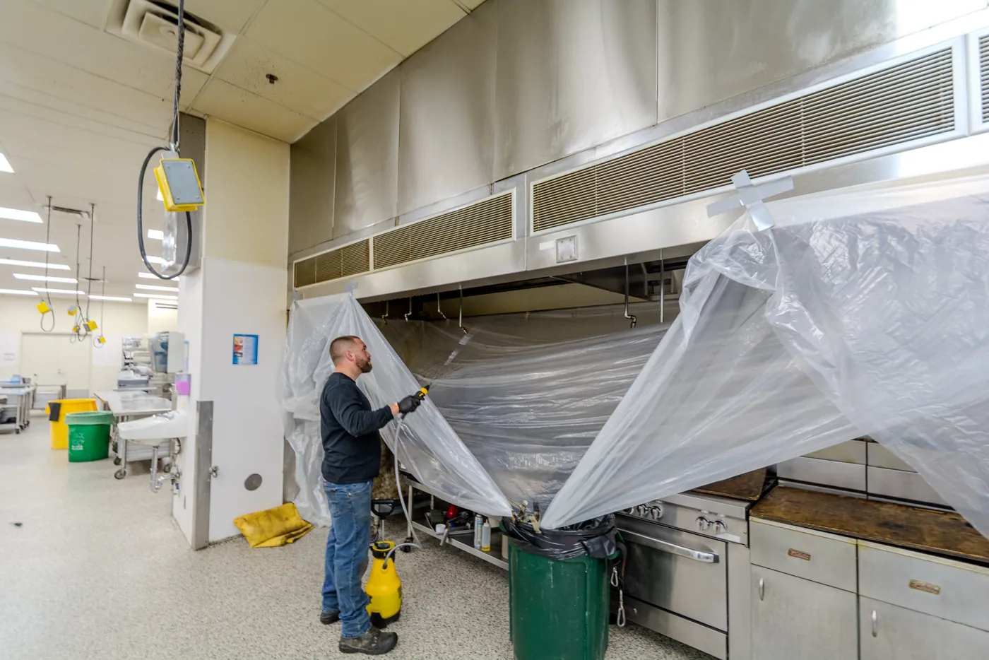 Technician spraying degreaser up into a hood plenum from inside the containment sheeting.