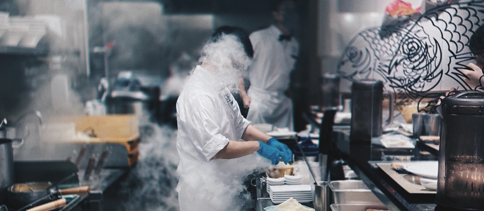 Chefs working in a steam-filled restaurant kitchen during service.