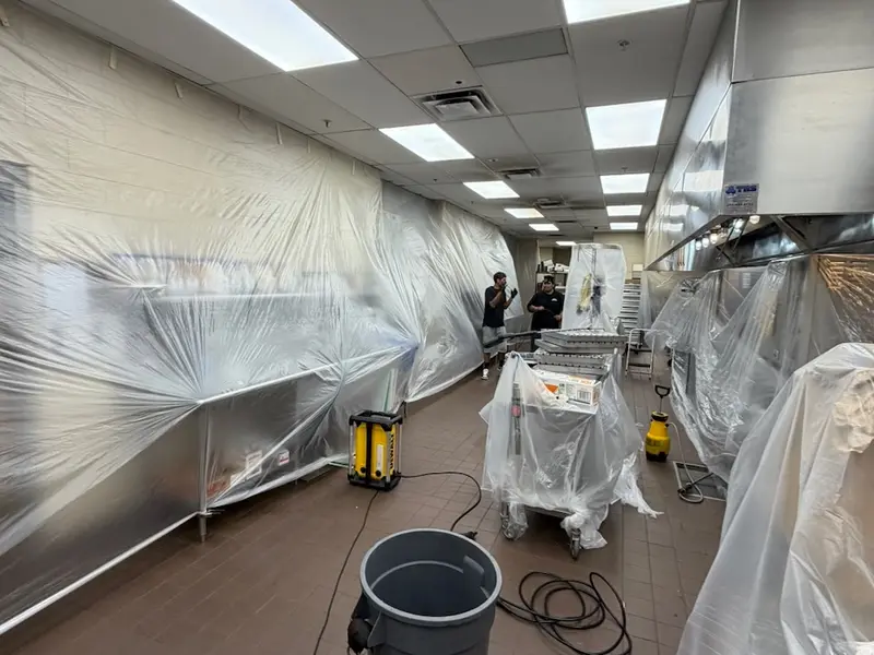 Commercial kitchen with the cook line and equipment covered in plastic sheeting for deep cleaning.